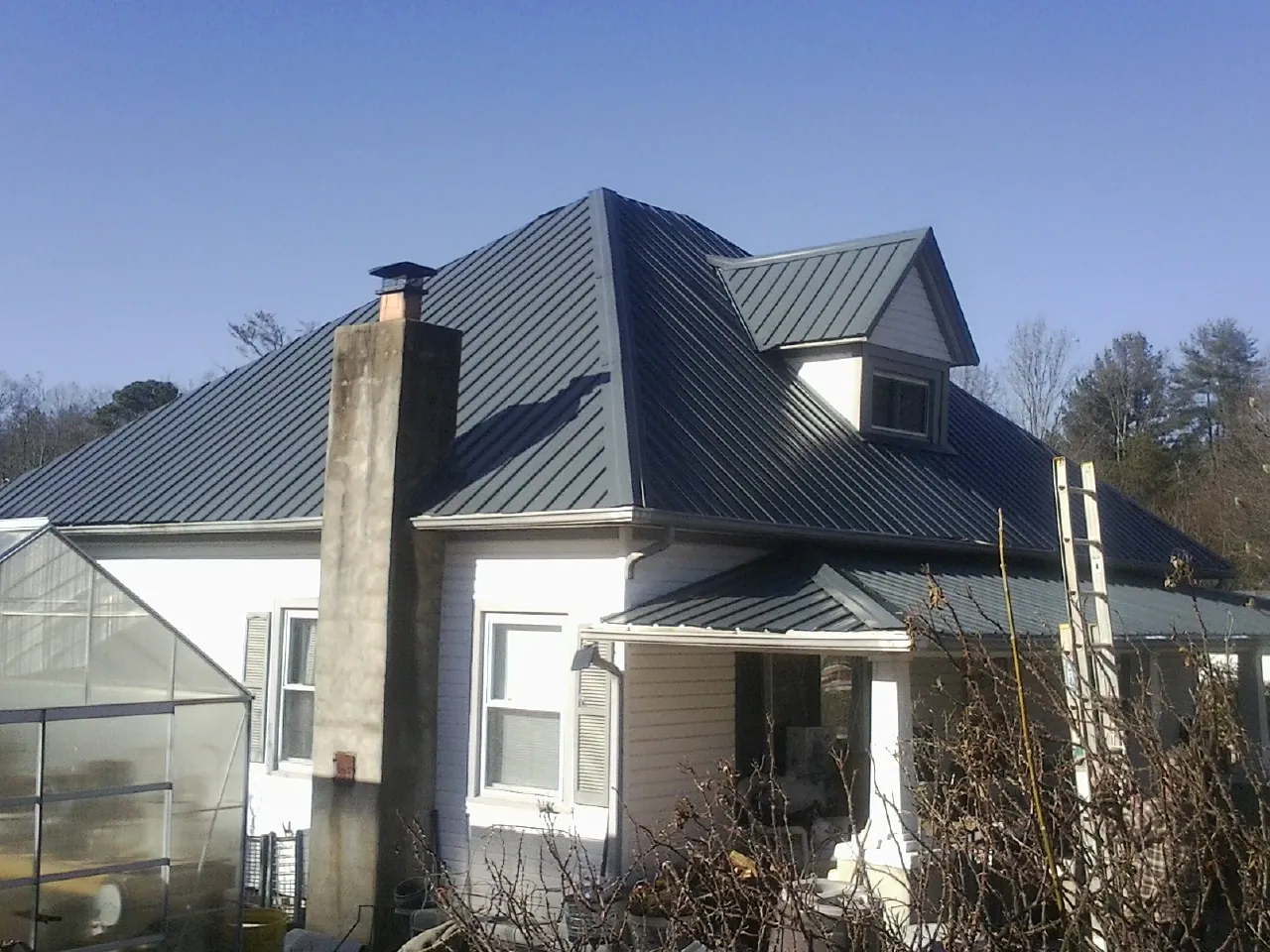 Dark blue standing seam metal roof on a white farmhouse with dormer — Slate & Tile Roof Repair by Roofing Brothers in Gregory