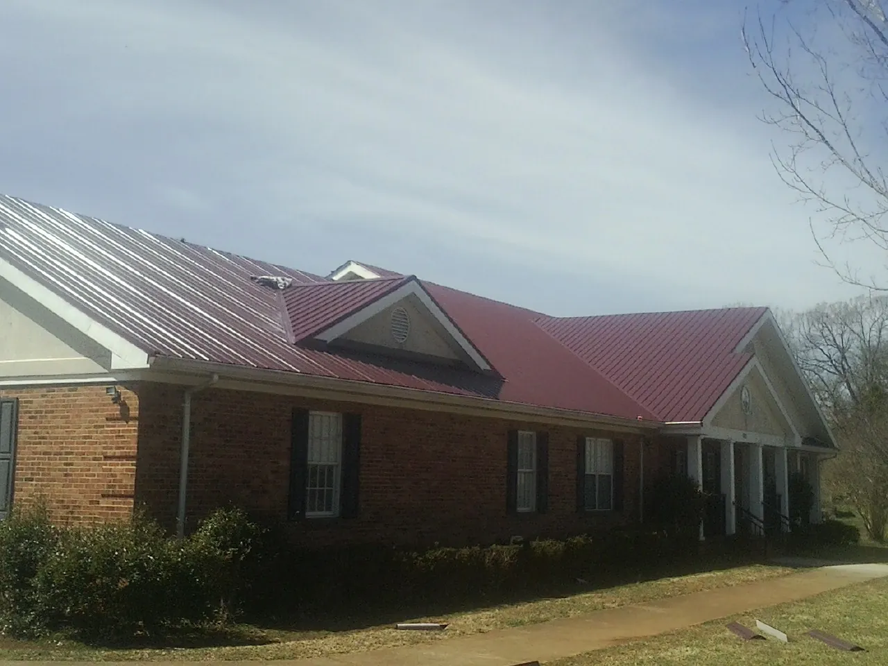 Red metal roof with gabled entries on a long brick building, from a Hail Damage Roof Repair job in Gregory