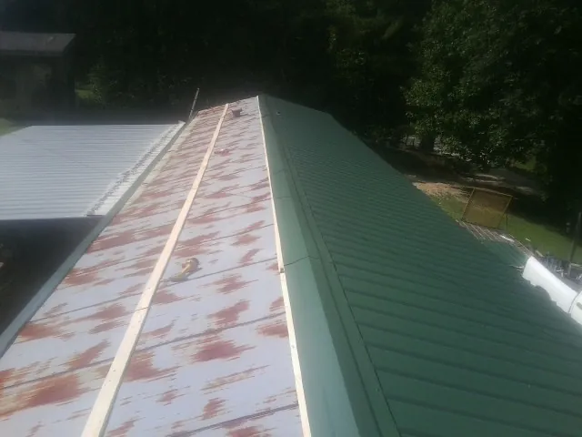 Old rusted panels beside newly installed green metal roofing — Wind Damage Roof Repair by Roofing Brothers in Gregory
