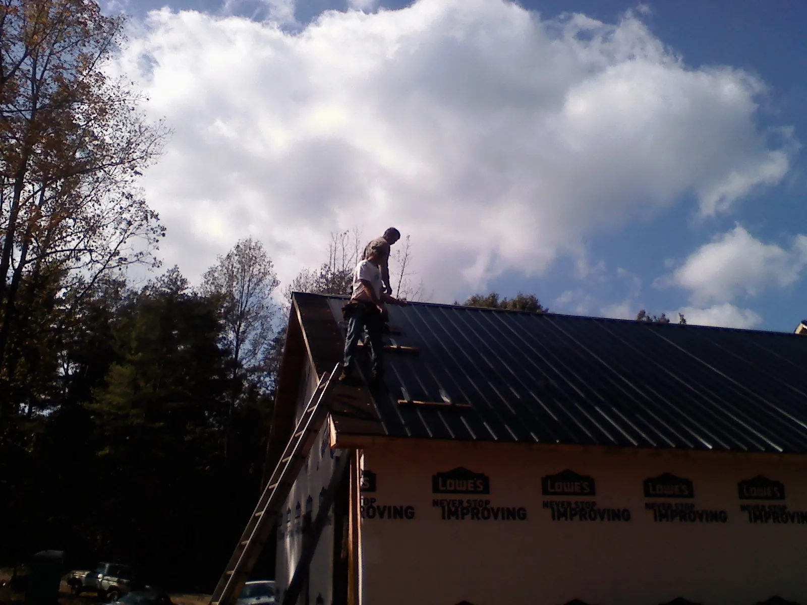 Roofer fastening dark metal panels high against a cloudy sky, from a Roof Inspection job in Gregory