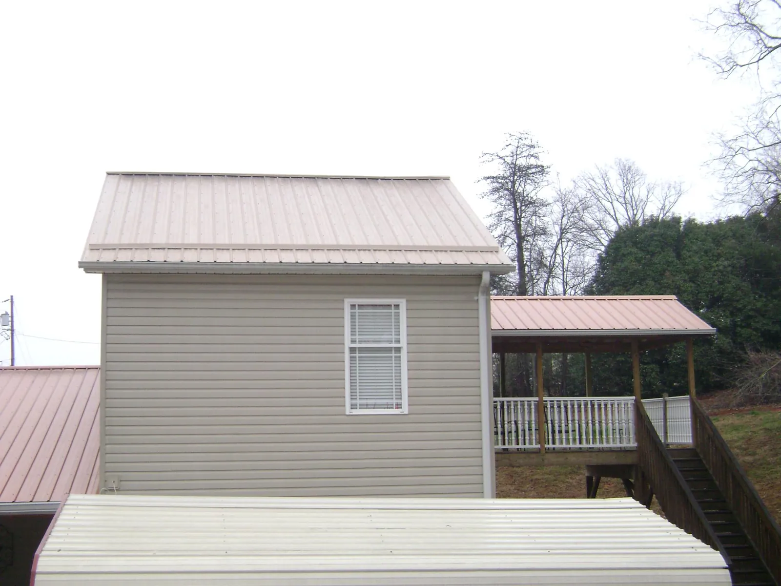 Tan metal roofs on a two story addition and attached porch, from a Roof Replacement job in Gregory
